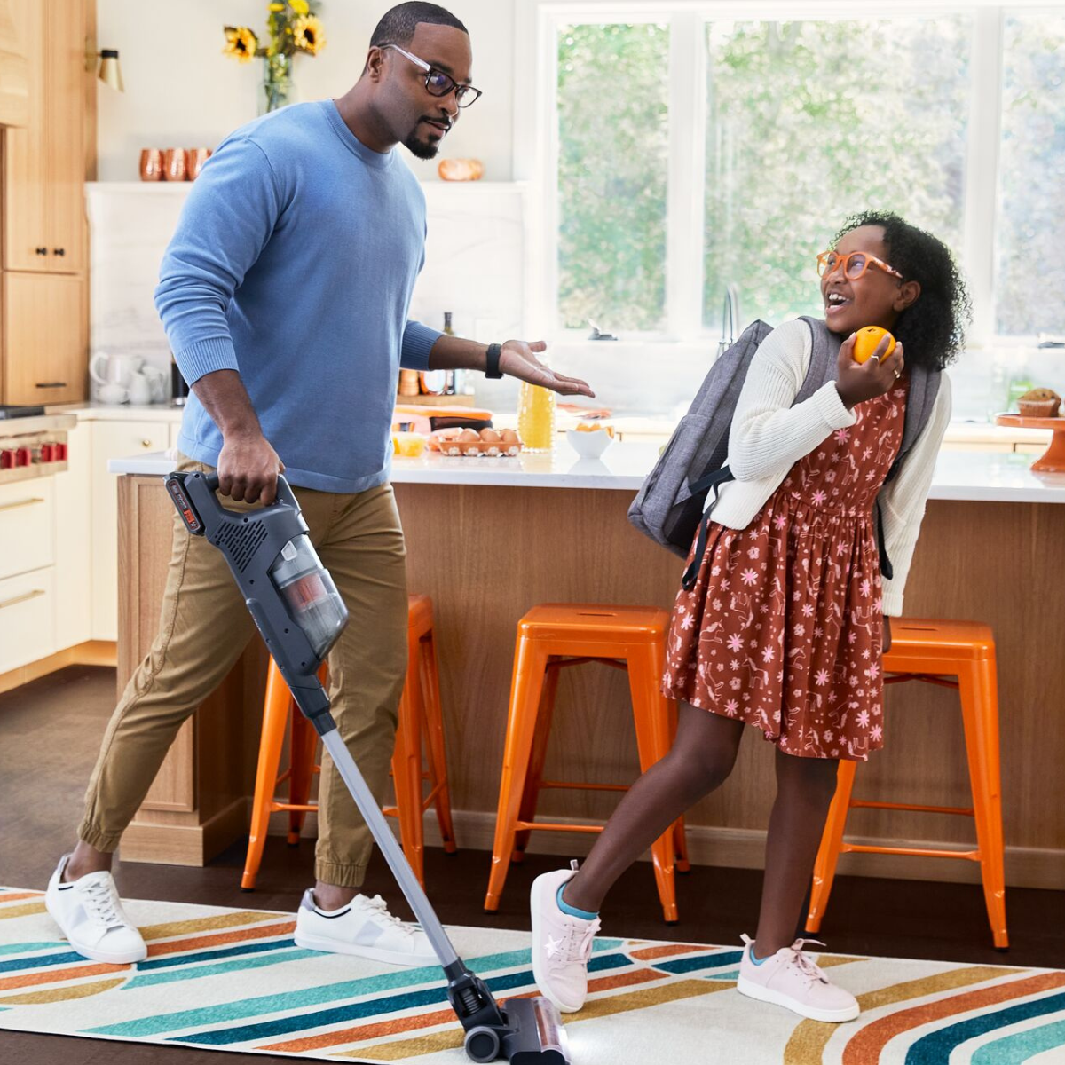 dad playfully chasing daughter with BLACK+DECKER Powerseries+ stick vacuum in kitchen