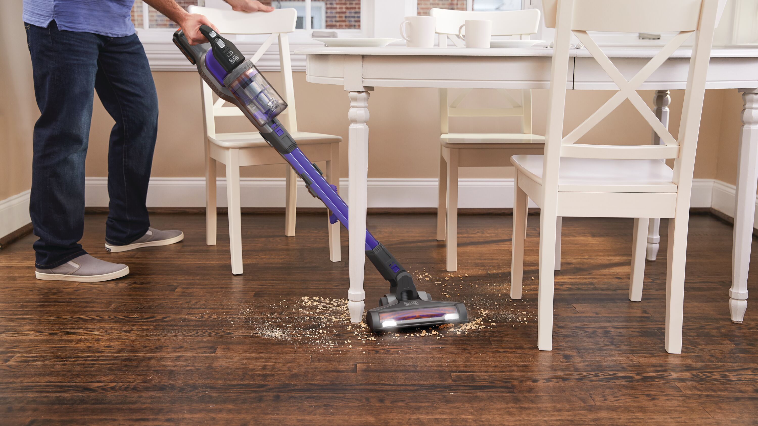 power series extreme pet cordless stick vacuum cleaner being used clean spilled material from the floor under a table.
