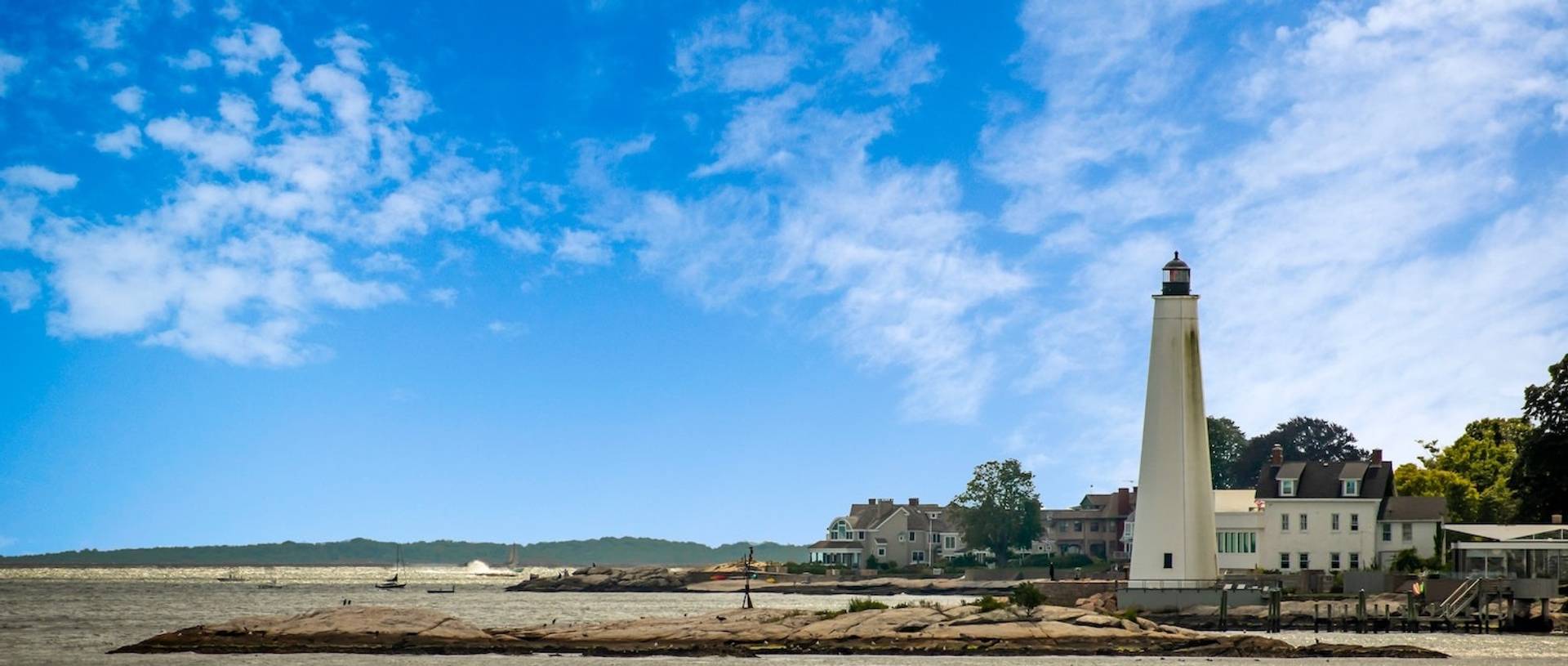 A bright blue sky behind a tall cream-colored lighthouse to represent where to buy e-bikes in Connecticut