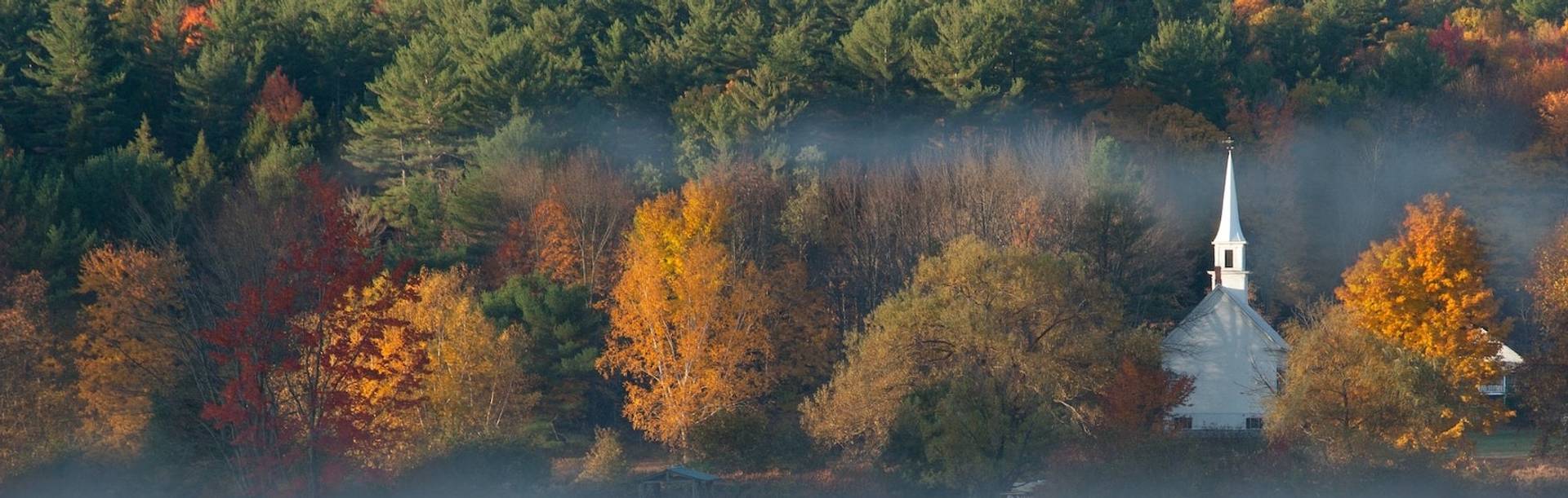 White church surrounded by colorful autumn trees to represent where to buy e-bikes in New Hampshire
