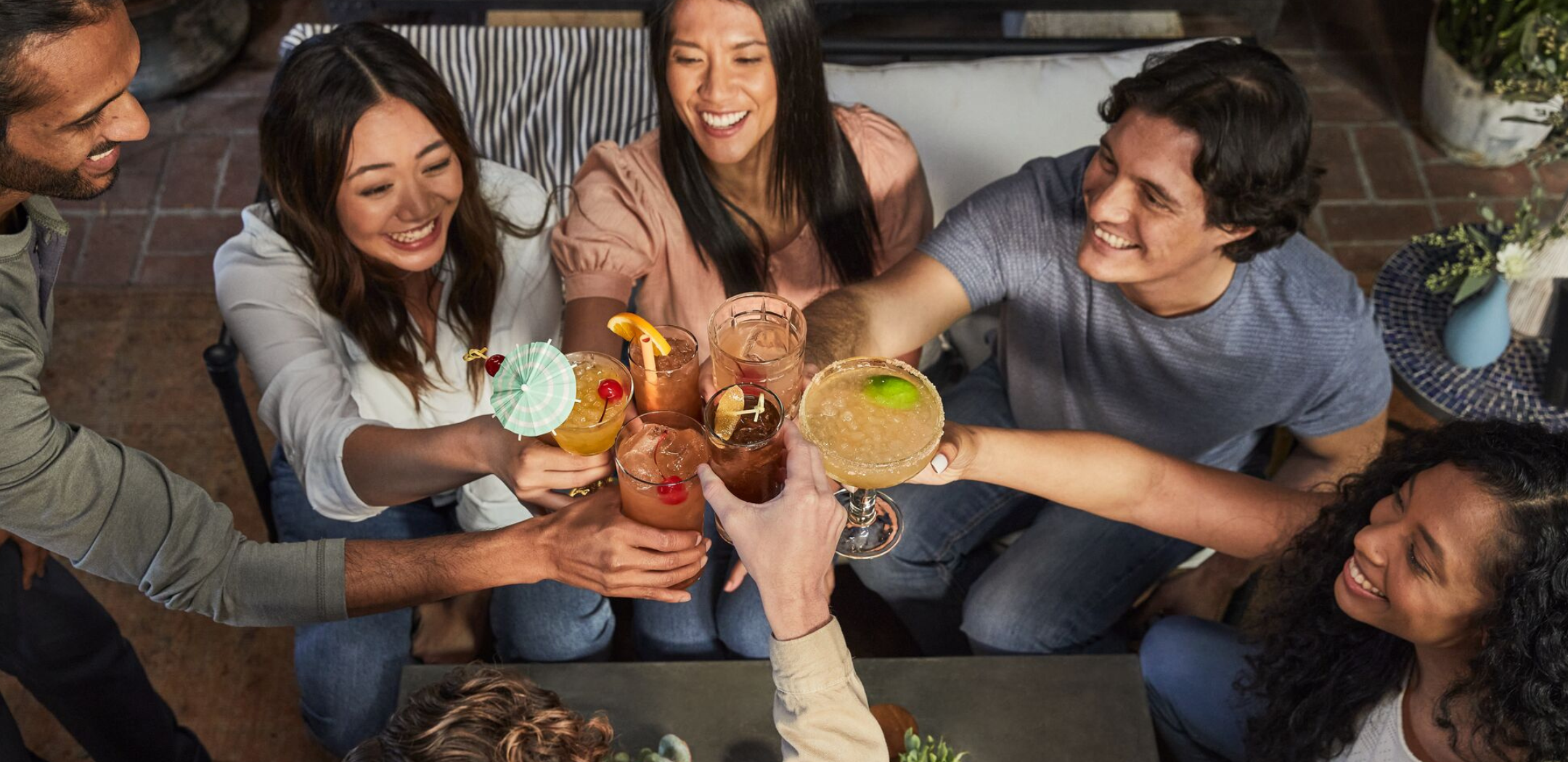 overhead view of a group of friends relaxing on a patio cheersing with their garnished cocktails