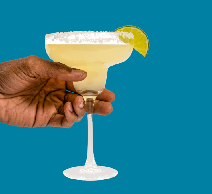 a hand holding a filled margarita glass with a lime slice on the rim