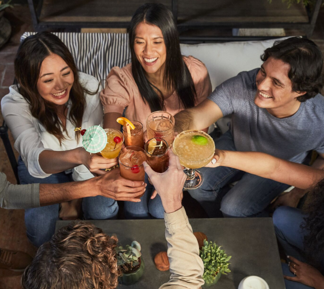 overhead view of a group of friends relaxing on a patio cheersing with their garnished cocktails