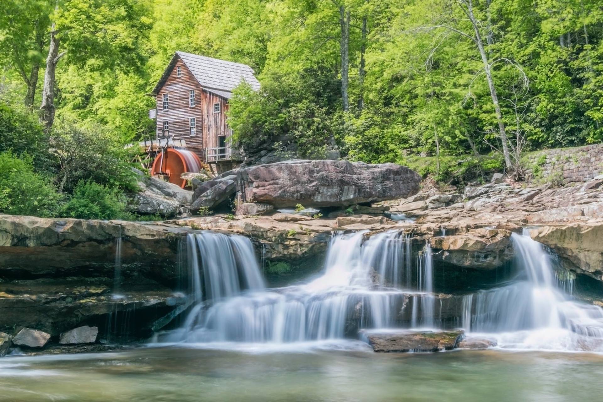 Rustic wooden building near waterfall amid lush green trees to represent where to buy e-bikes in West Virginia