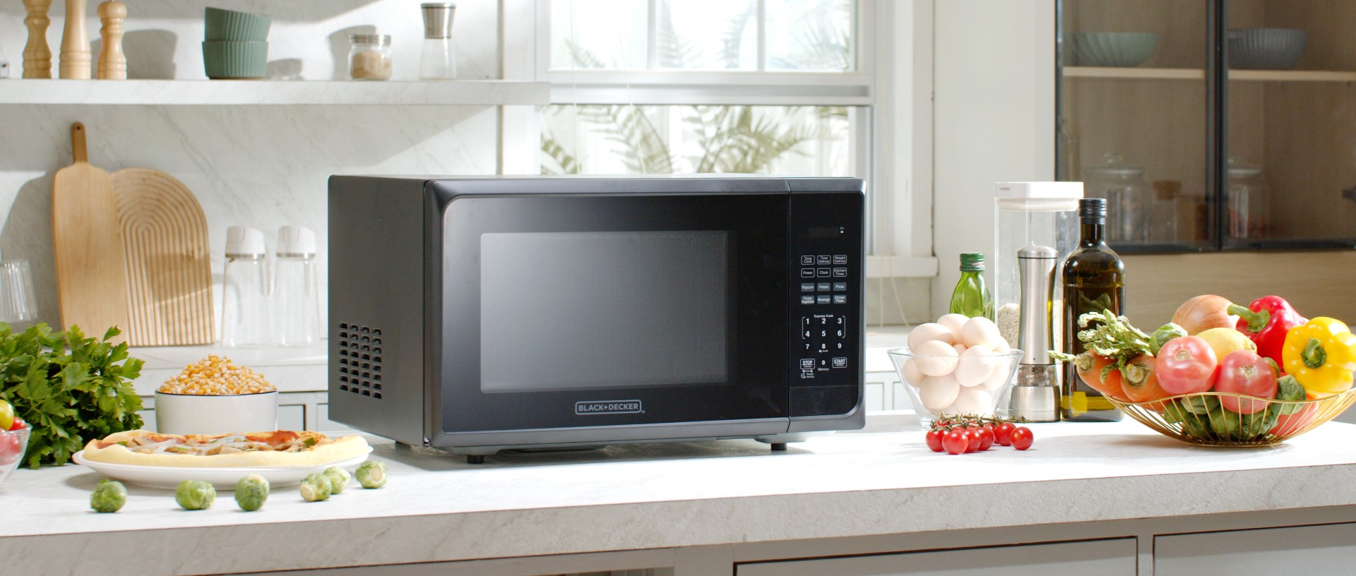 BLACK+DECKER microwave sitting on top of a white kitchen counter with various food items around it.