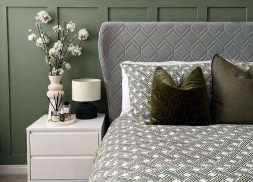 A green duvet cover set with an abstract basket weave design, arranged on a bed with olive green cushions next to a decorated side table.
