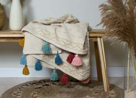 cream throw draped on a wooden bench, multi coloured tassels
