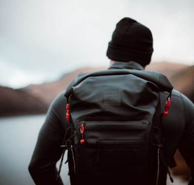 Man wearing Red Equipment Voyager Beanie in Charcoal, Long Sleeve Performance Top Layer and carrying the Adventure Waterproof Backpack in Obsidian Black looking over a lake in the Lake District.