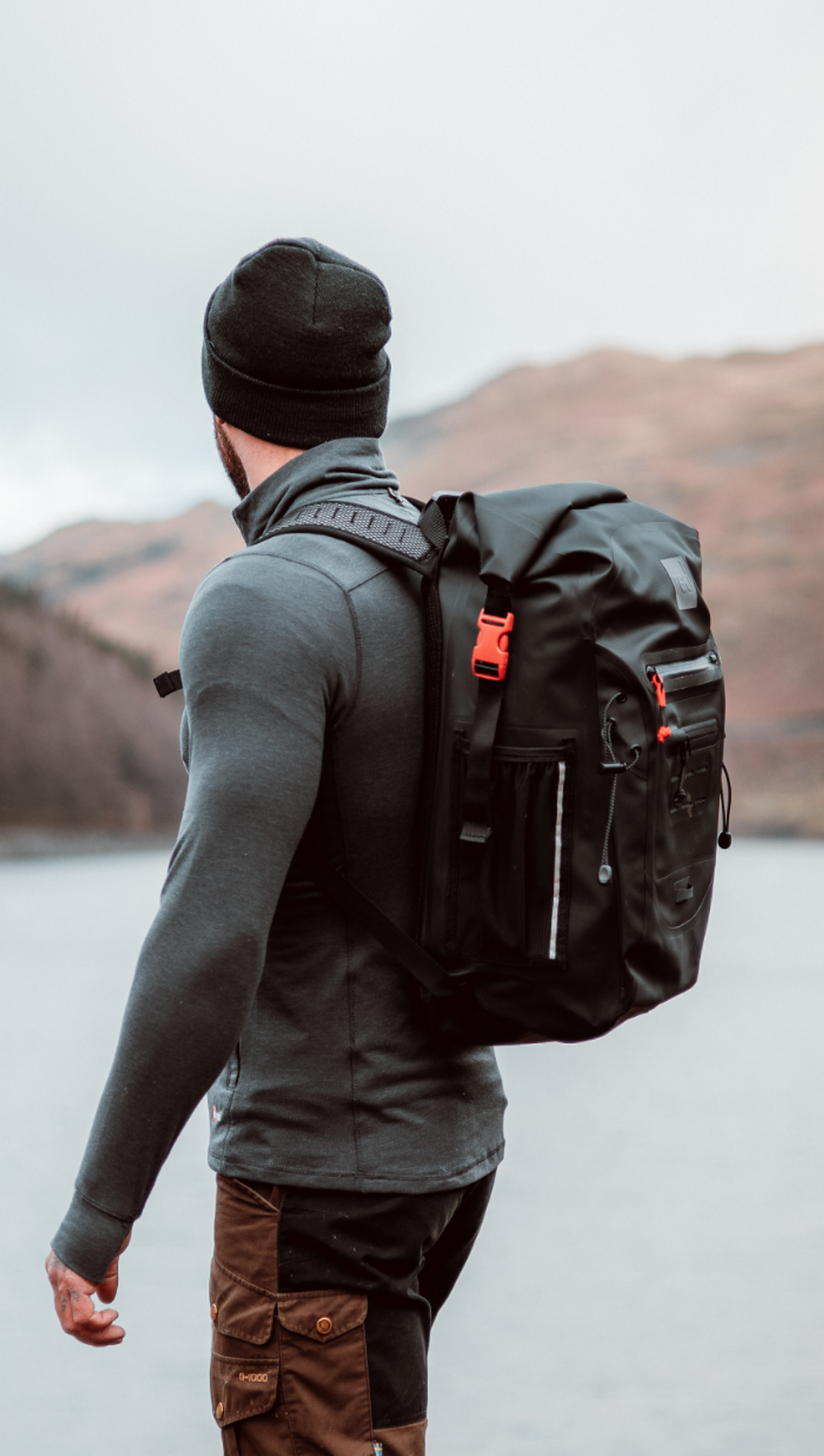 Man wearing Red Equipment Performance Long Sleeve Top and Voyager Beanie in Charcoal, carrying Adventure Waterproof Backpack in Obsidian Black