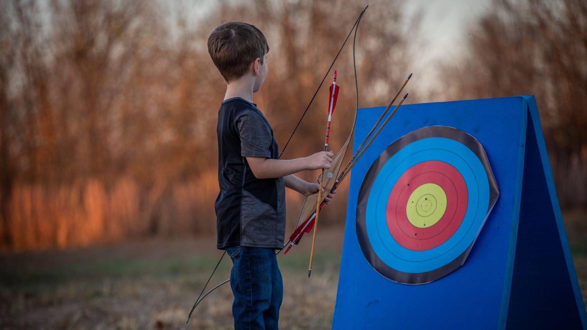 Little boy holding a Bear Archery Little Bear Recurve Bow with arrows in his hand