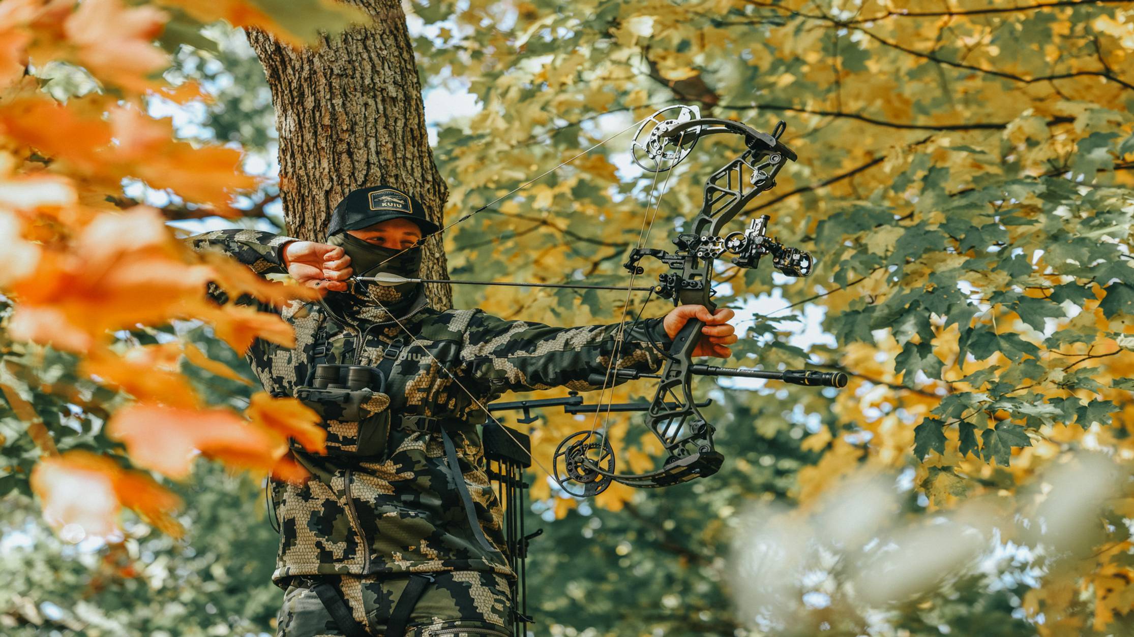 Man in tree stand with the Bear Archery Persist compound bow at full draw.