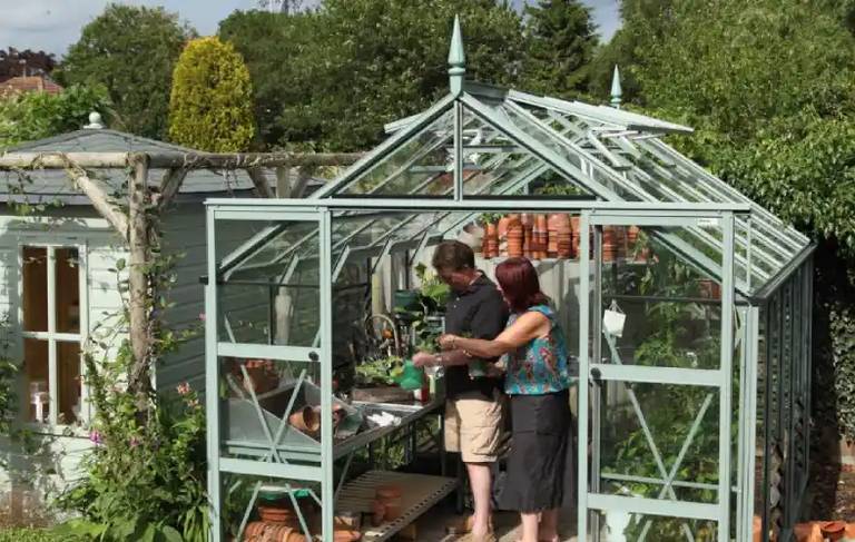 A couple in their Rhino greenhouse next to a summer house