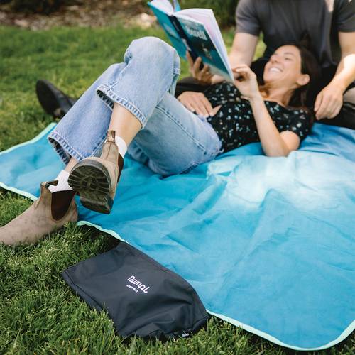 Woman uses a Rumpl Everywhere Mat as a waterproof park mat as she lays down on the grass to read a book.