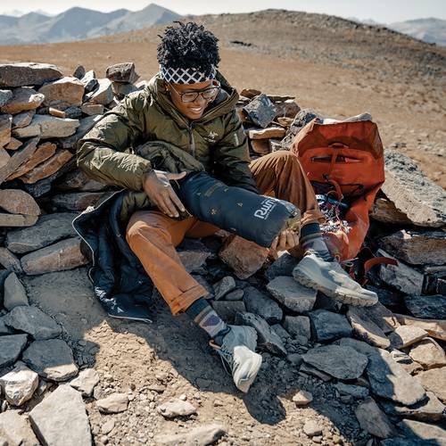 person sitting on some rocks and stuffing a nanoloft puffy blanket back into its stuff sack