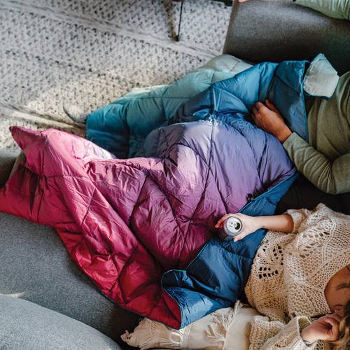 top view of two people's legs as they lounge on a couch with a NanoLoft® Puffy Blanket spread out across their legs