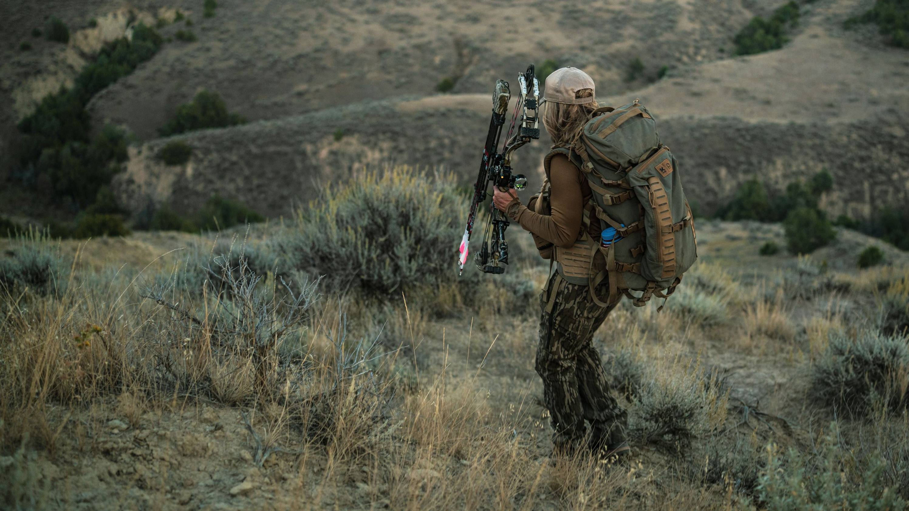 Woman walking down a hill carrying the Resilient RTH short draw compound bow from Bear Archery.