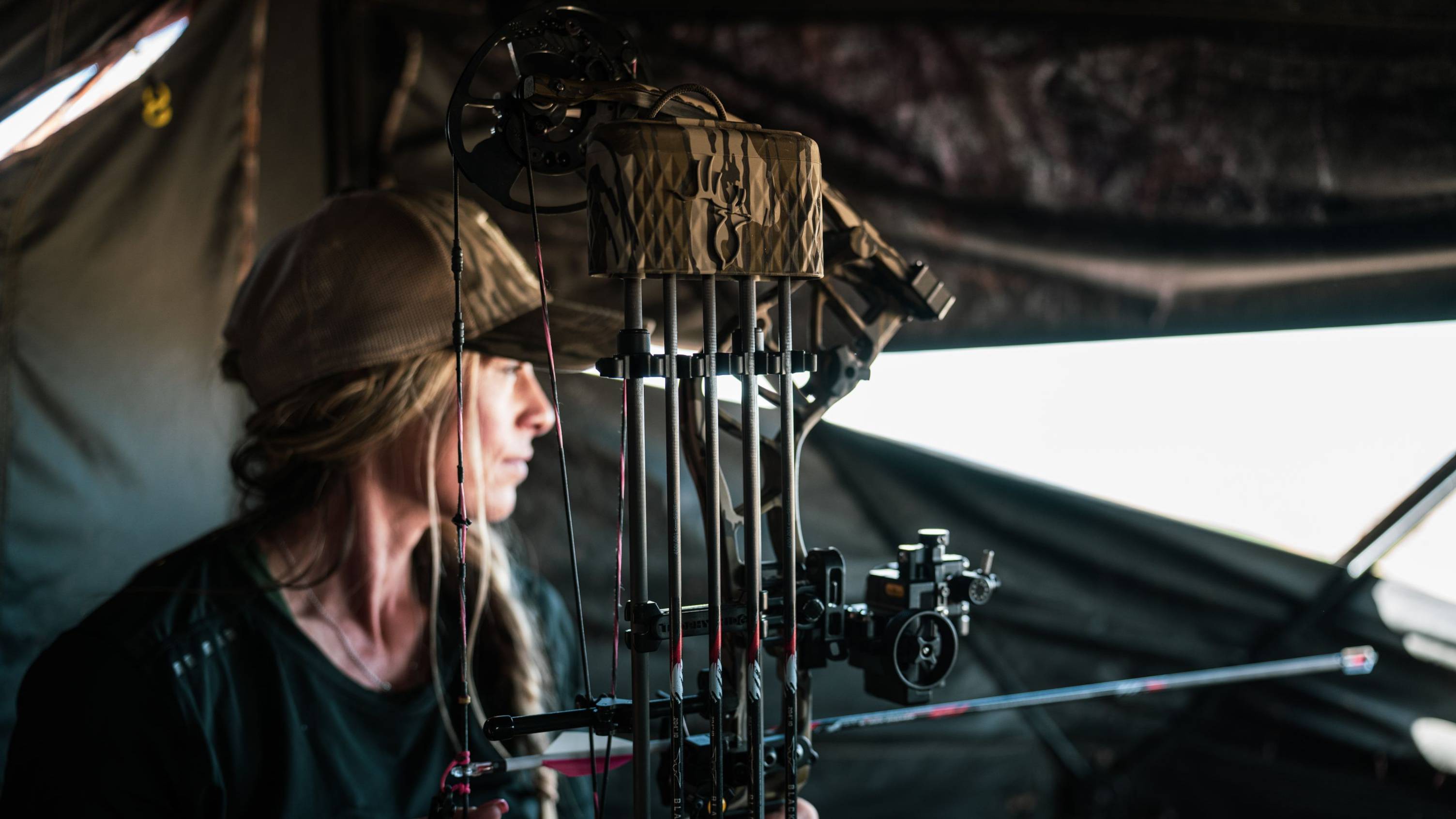 Woman sitting in a hunting blind with the Bear Resilient RTH short draw compound bow.