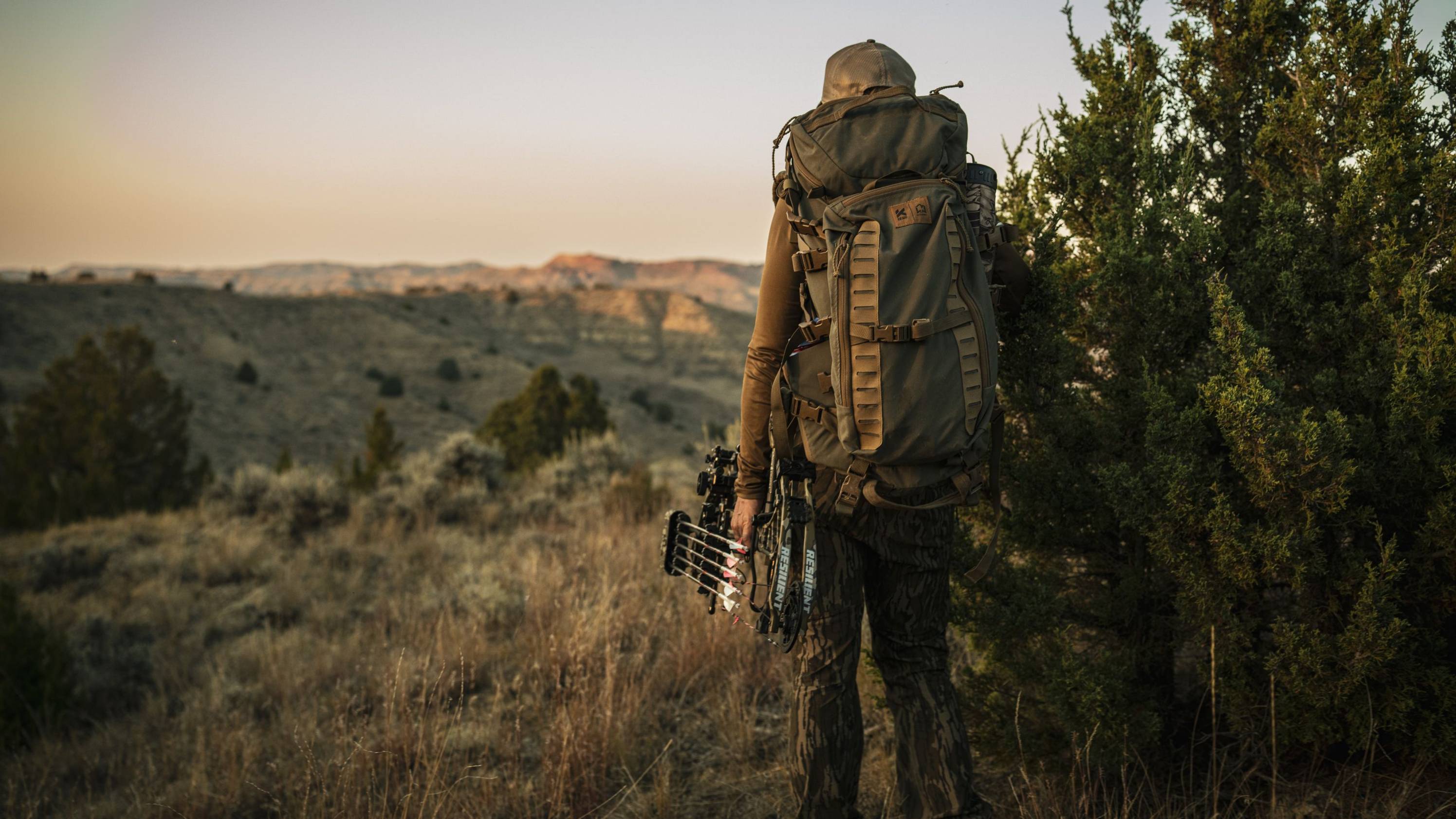 Woman holding a Resilient RTH short draw compound bow from Bear Archery looking at the sunset.