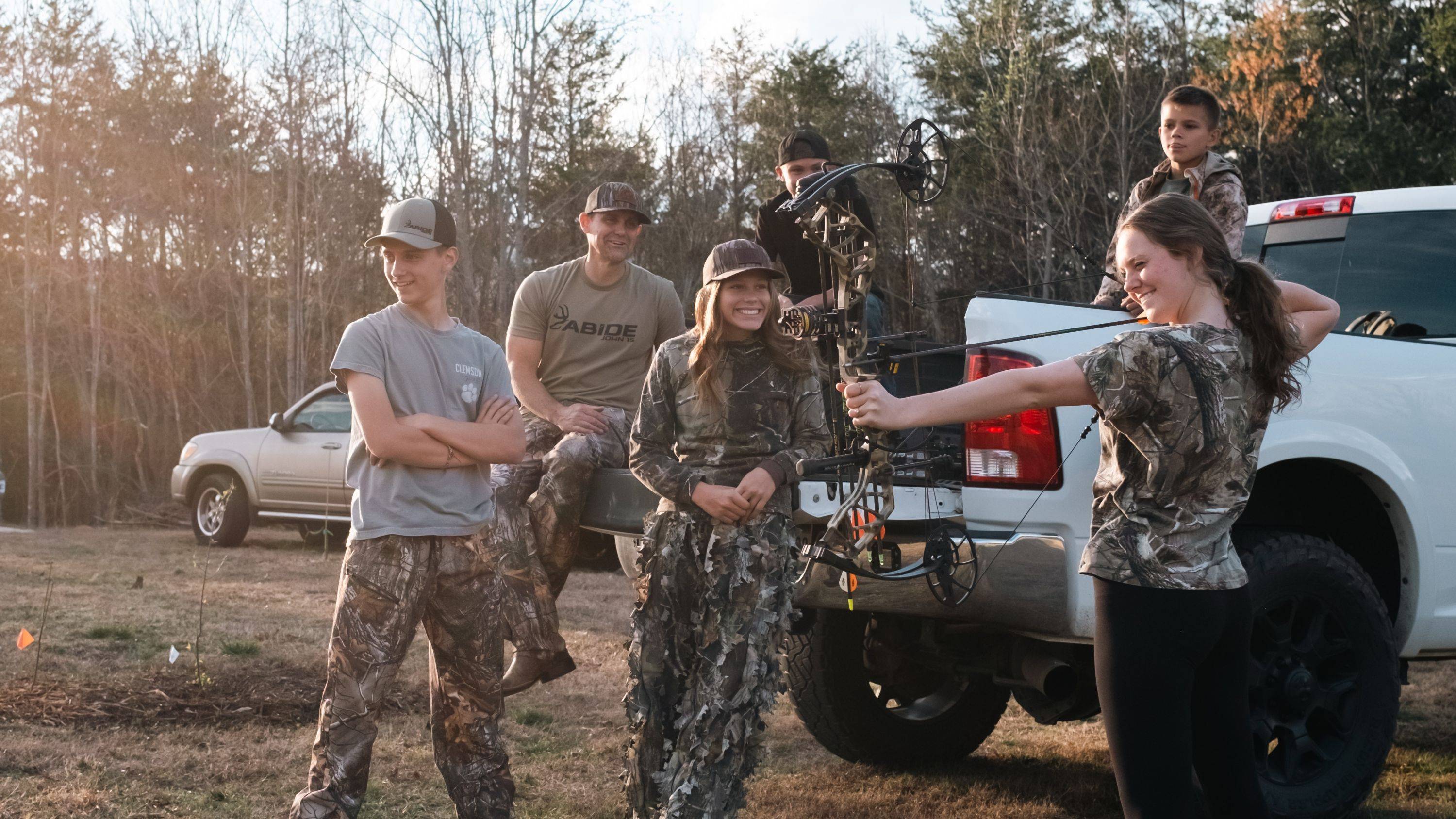 Woman shooting a Bear Legit MAXX compound bow from Bear Archery surrounded by friends.
