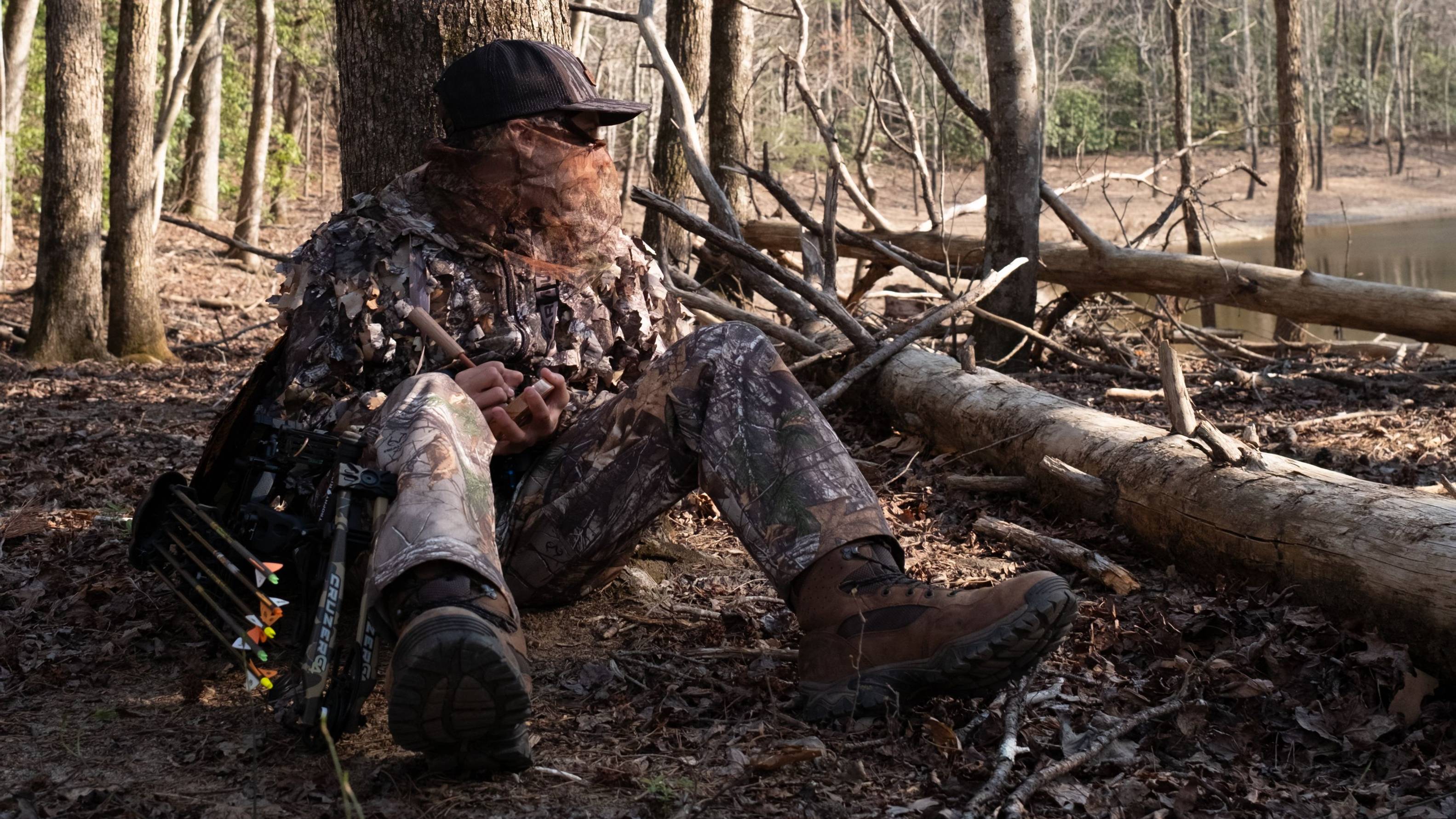 Man sitting in the woods with a Cruzer G4 compact compound bow from Bear Archery.