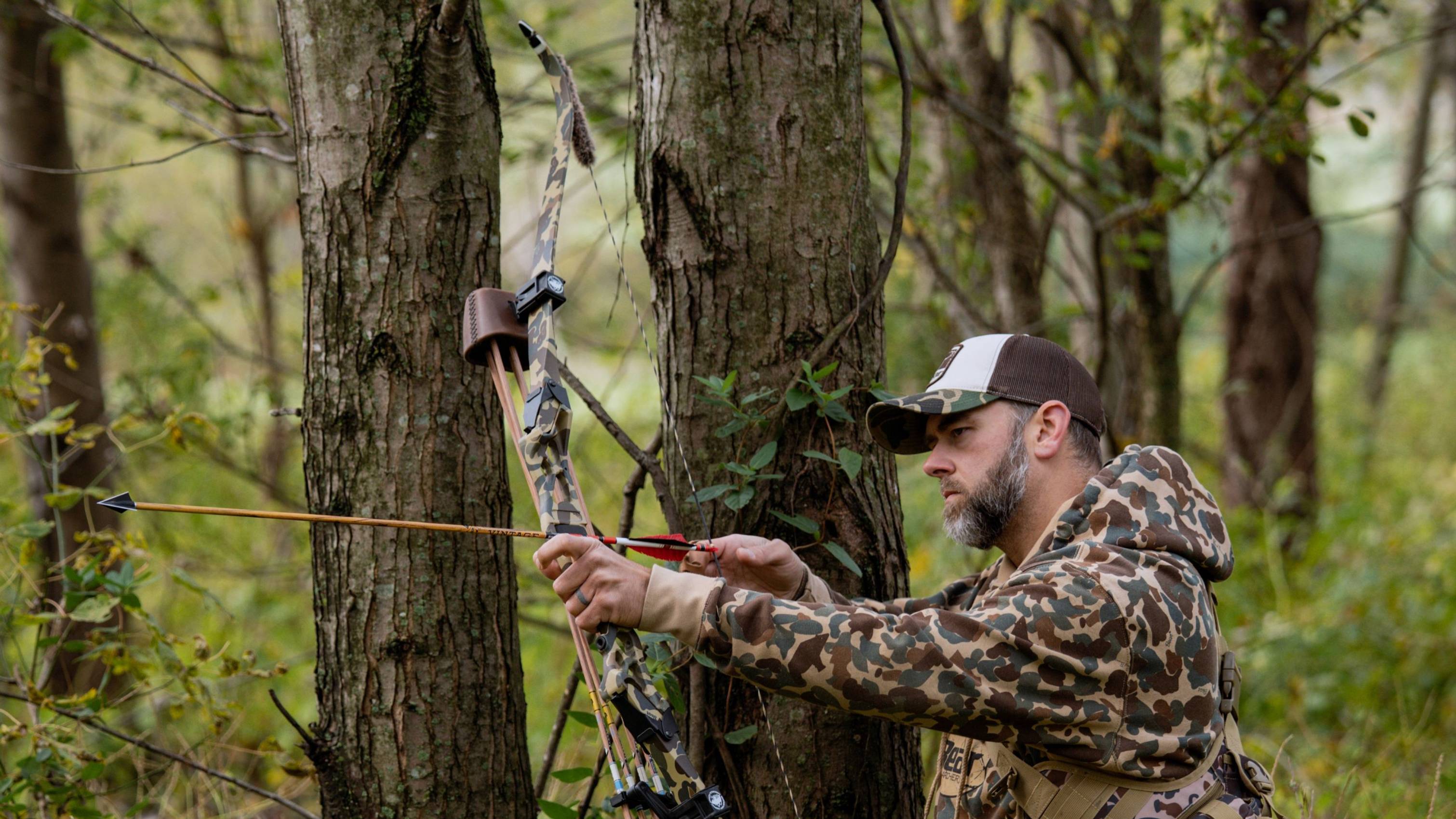 Man in the forest using a takedown recurve bow with Fred Bear Camo Take Down Limbs from Bear Archery.