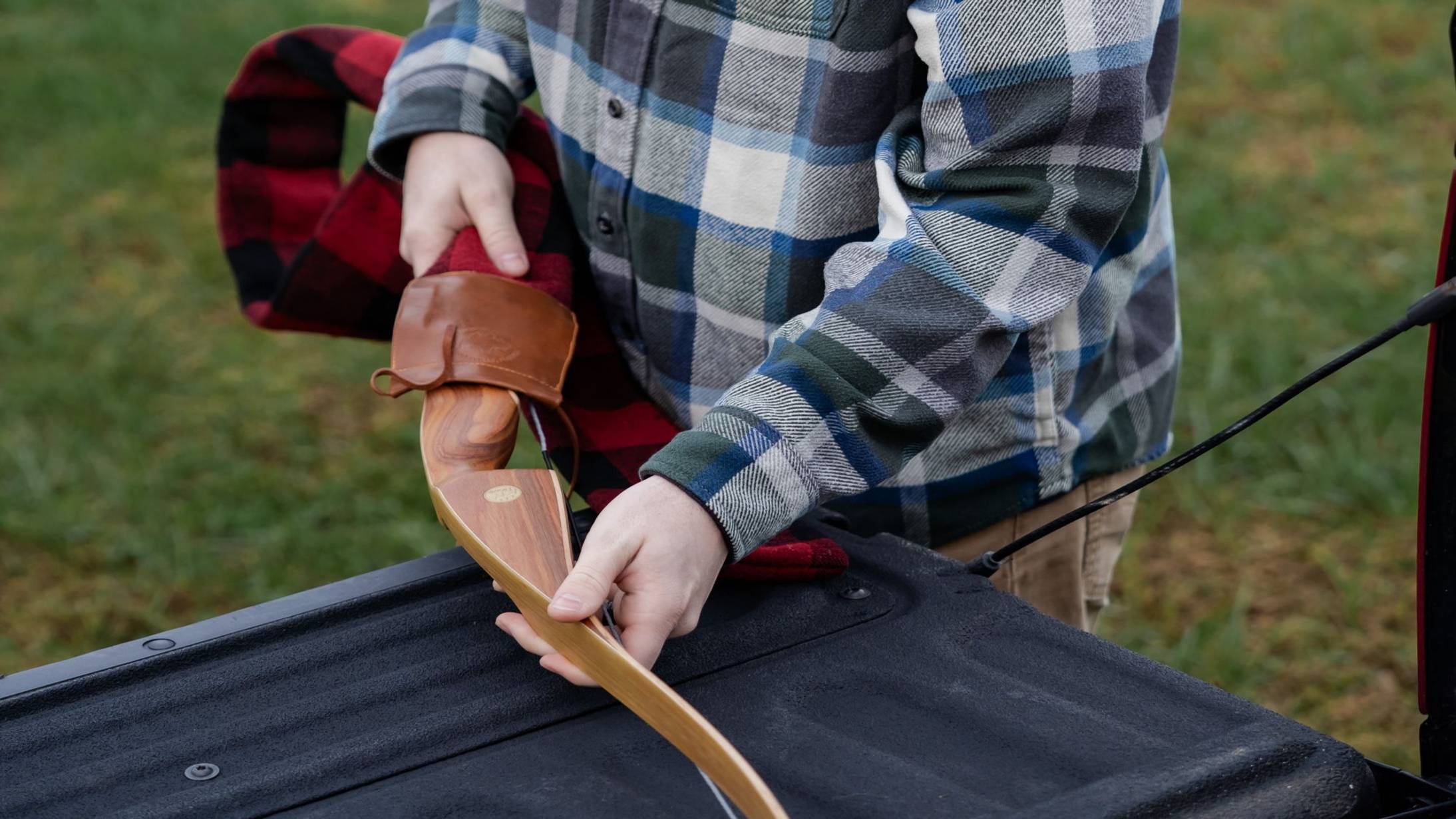 Man removing Grizzly Hunter Hybrid Longbow from Bear Archery from a plaid bow sock.