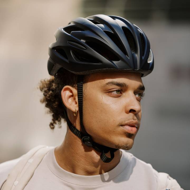 A person wearing a black Silas Road Bike Helmet, with curly hair peeking out, dressed in a light-colored, casual shirt.