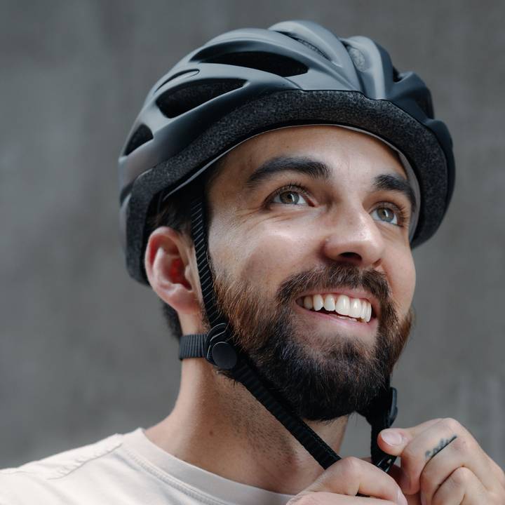 A person smiles while adjusting the chin strap on of their Silas Bike Helmet.