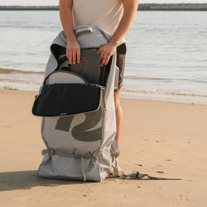 A person at the beach opens a grey backpack to reveal paddles inside, ready for a day of water activities.