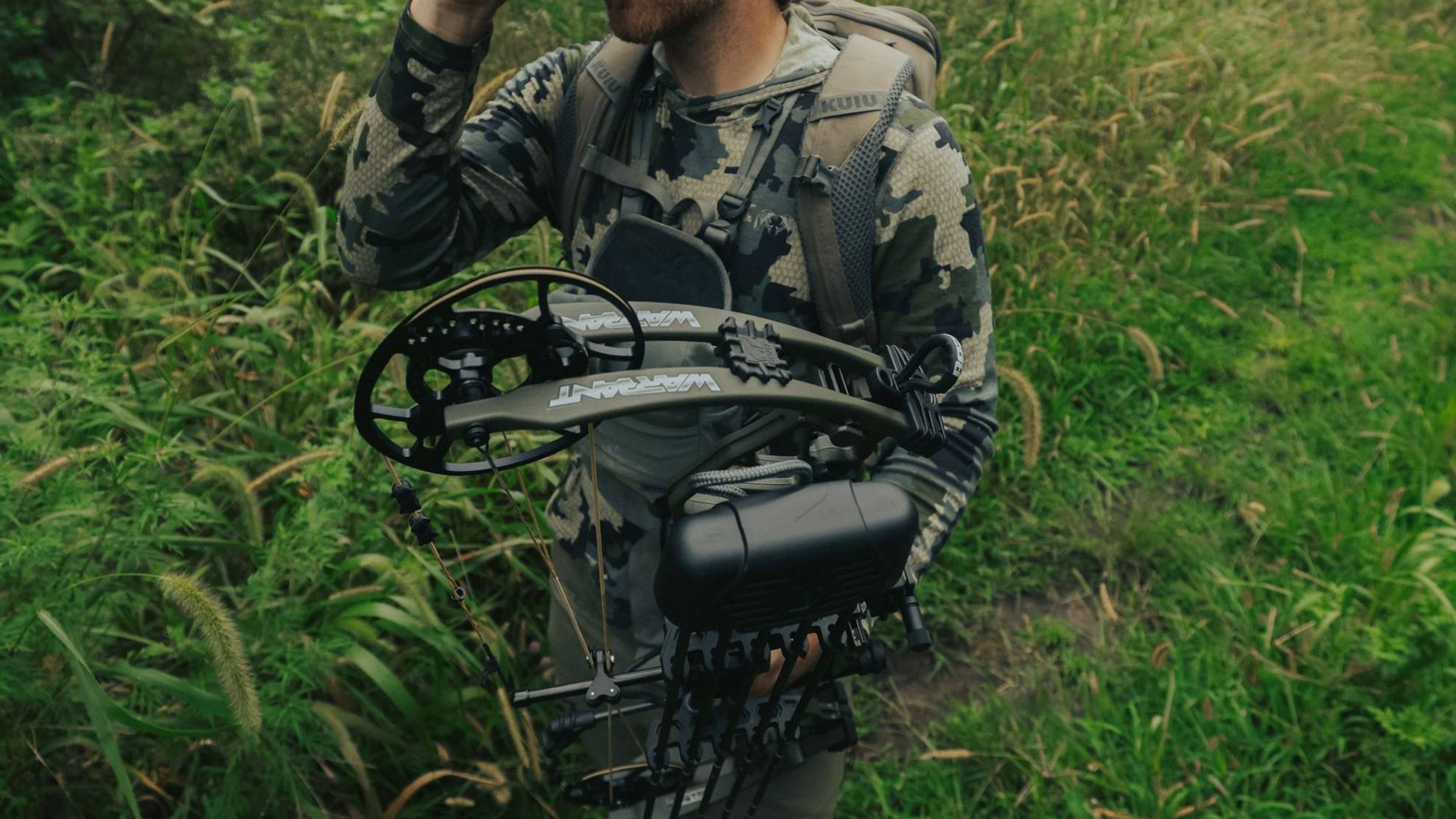 Man hunting in a field with the Warrant RTH compound bow from Bear Archery.