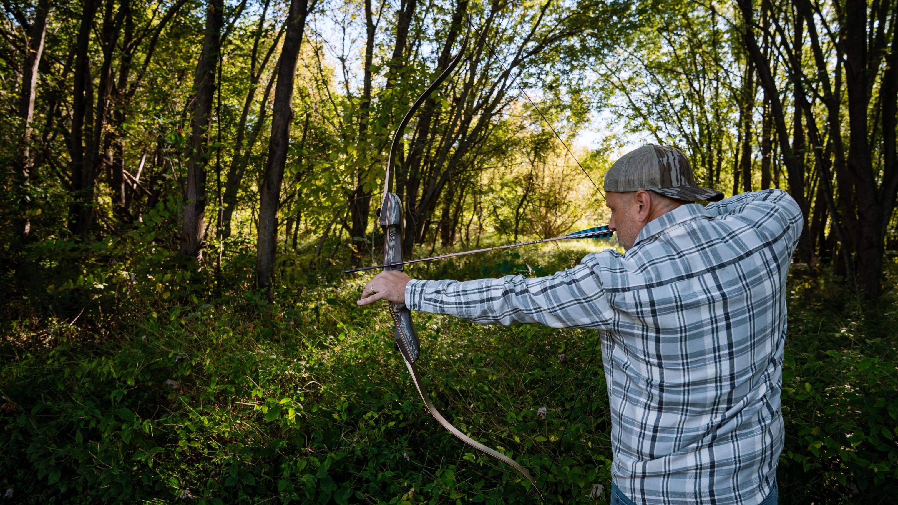 Man shooting the Wolverine X recurve bow from Bear Archery in the woods.