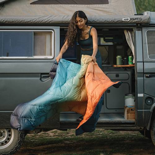 a woman standing on a camper van, dusting out her Rumpl NanoLoft® Puffy Blankets