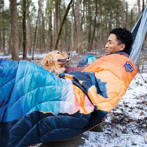 A man and his dog relaxing on a hammock outdoors with a Rumpl National Parks Blanket