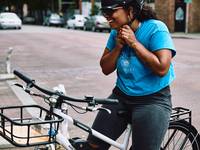 A woman of color clips her helmet on as she sits on a white RadMission electric bike.