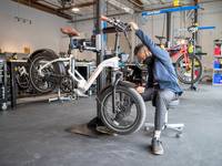 A Rad Power Bikes employee is inspecting a white Rad City 3 Step-Thru that is on a maintenance rack.
