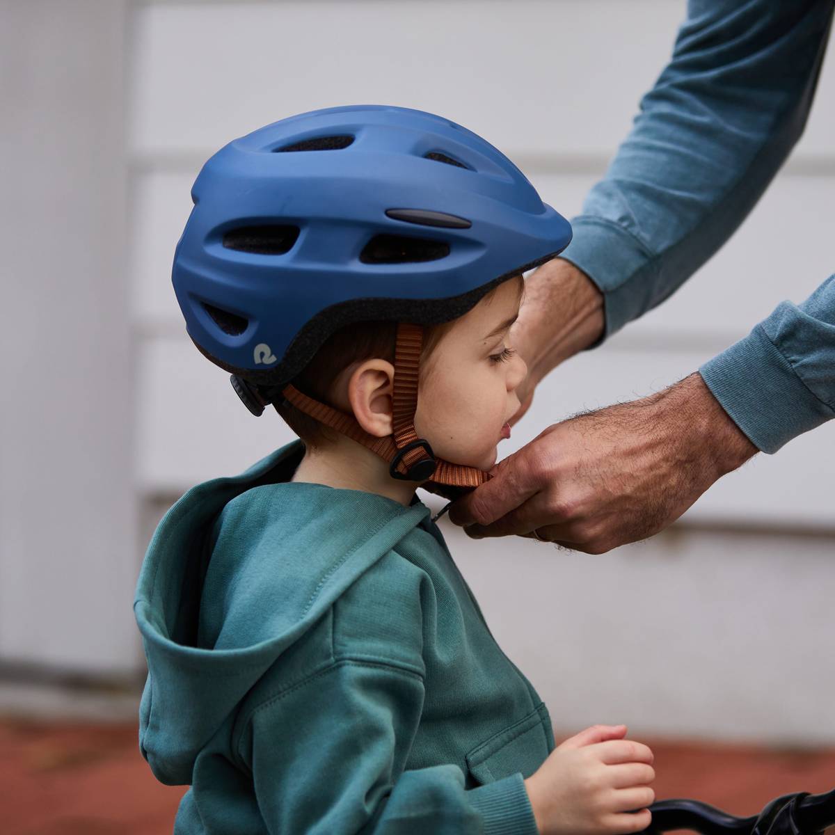 A child in a blue helmet receives assistance from an adult while preparing for an outdoor activity, showcasing a moment of care and safety.