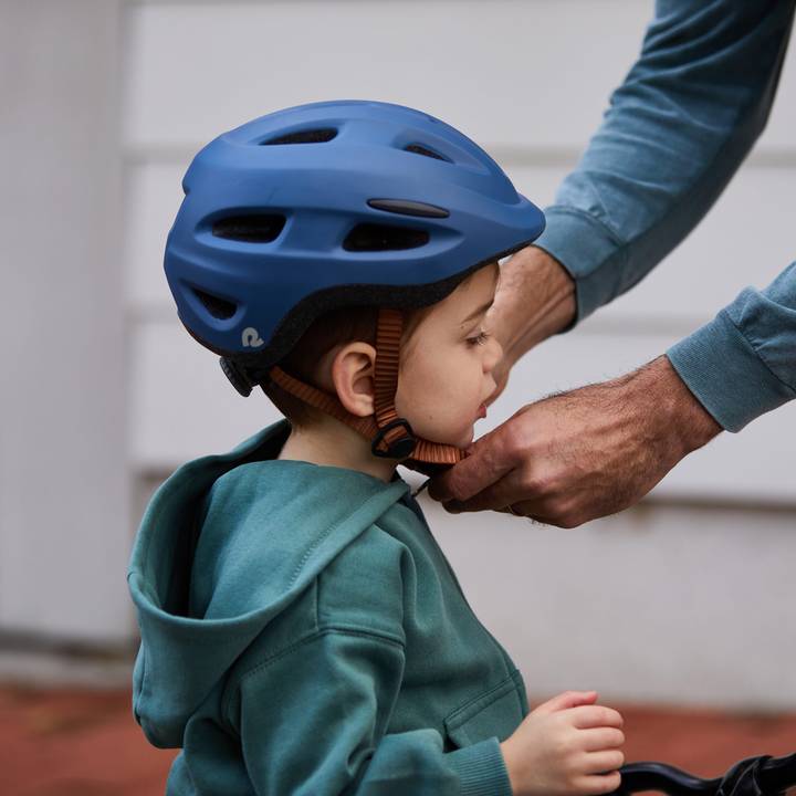 A child in a blue helmet receives assistance from an adult while preparing for an outdoor activity, showcasing a moment of care and safety.