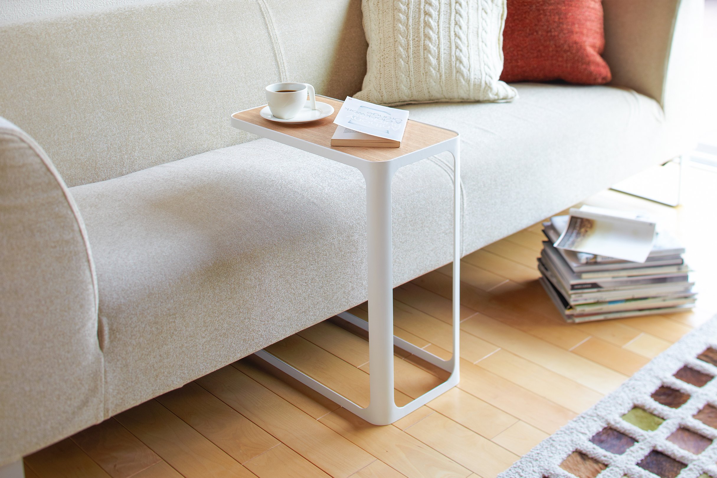 Yamazaki Home C Side Table holding a coffee cup and a book next to a sofa. 
