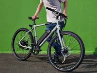 A light-skinned man stands in front of a green wall with his gray RadMission Electric Bike.