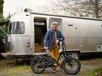A man with gray hair stands outside of his Air Stream with his RadExpand electric bike.