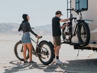 A person adjusting an electric bike on an RV rack, with another person standing by with another electric bike. 