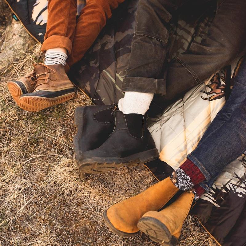 top view of three friends' feet crossed as they sit atop a Rumpl National Park blanket on the grass