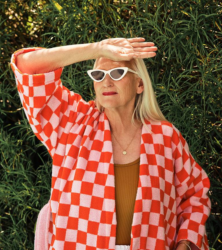 Woman shielding her eyes from the sun, wearing our new Checkerboard robe in Pop Pink.