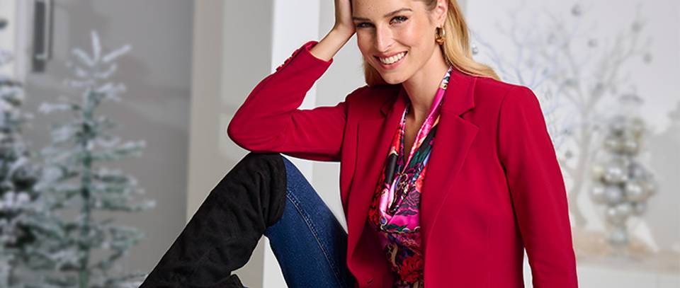 model wearing a red blazer, pink printed cowl neck charmeuse blouse, dark wash jeans, black over-the-knee suede boots, and gold hoop earrings.