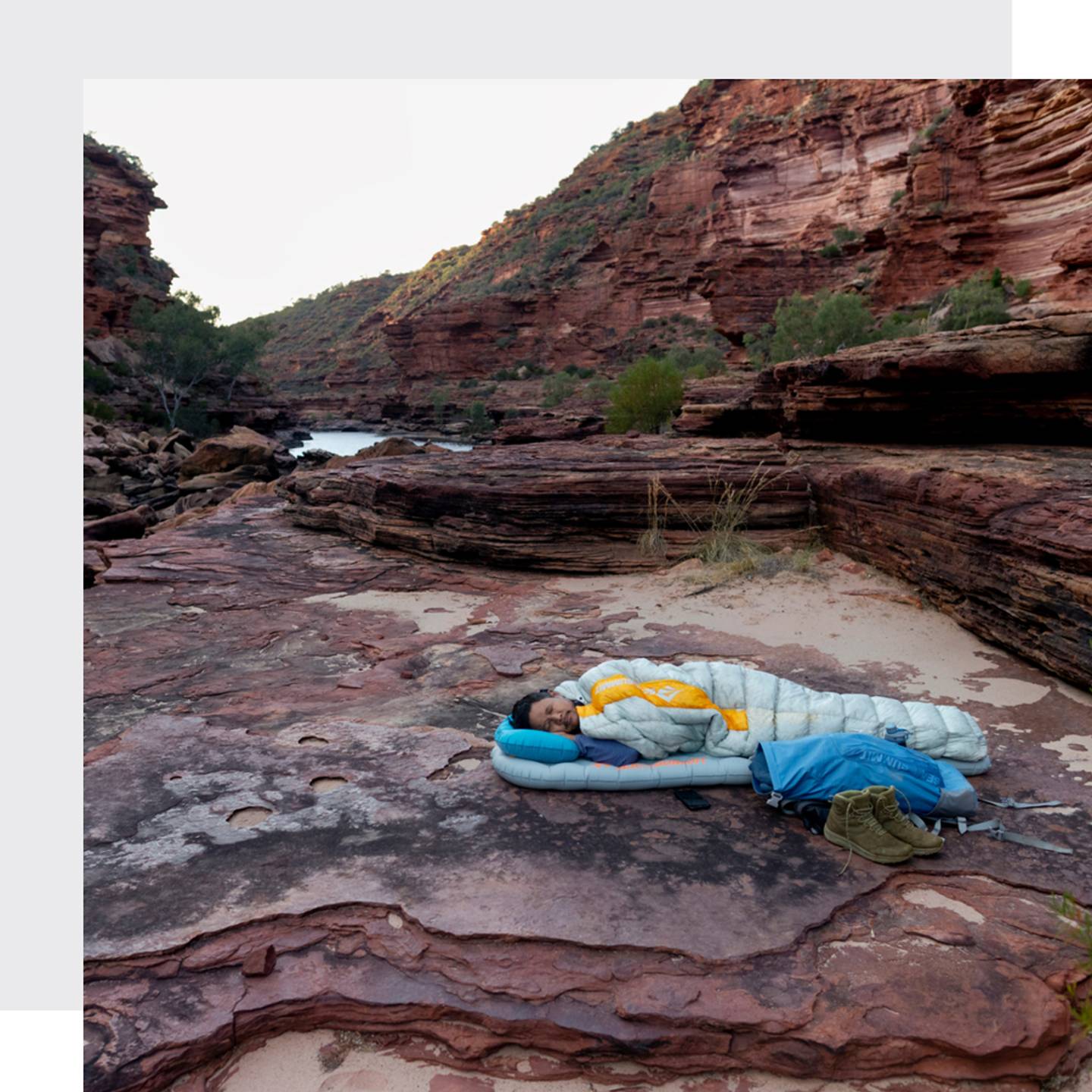 A man sleeping in his sleeping bag on a mat on a rocky ground in an australian canyon at the end of a exhausting day