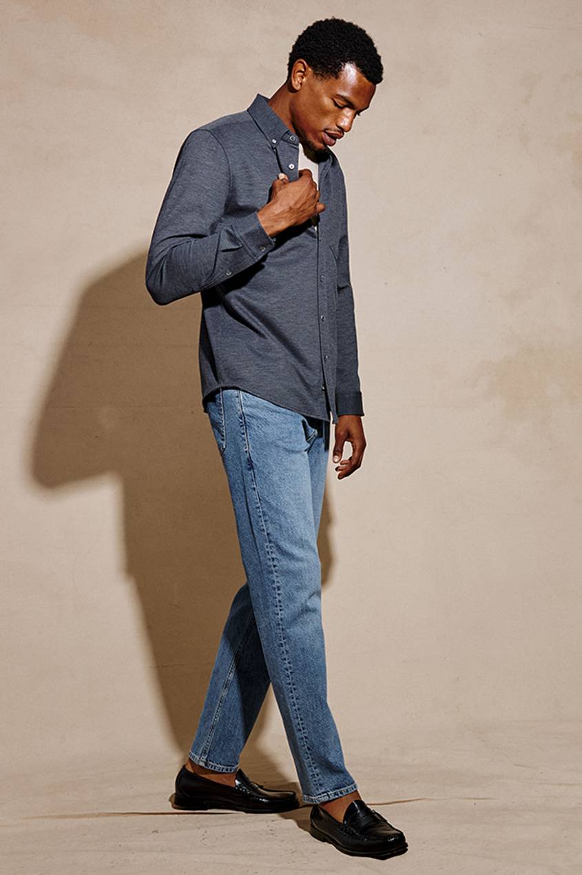 Man wearing a blue long sleeve shirt with blue jeans posed against a beige background.