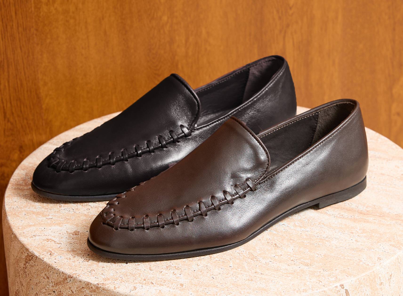 Pair of black and brown loafers on a textured surface with a brown wooden background.