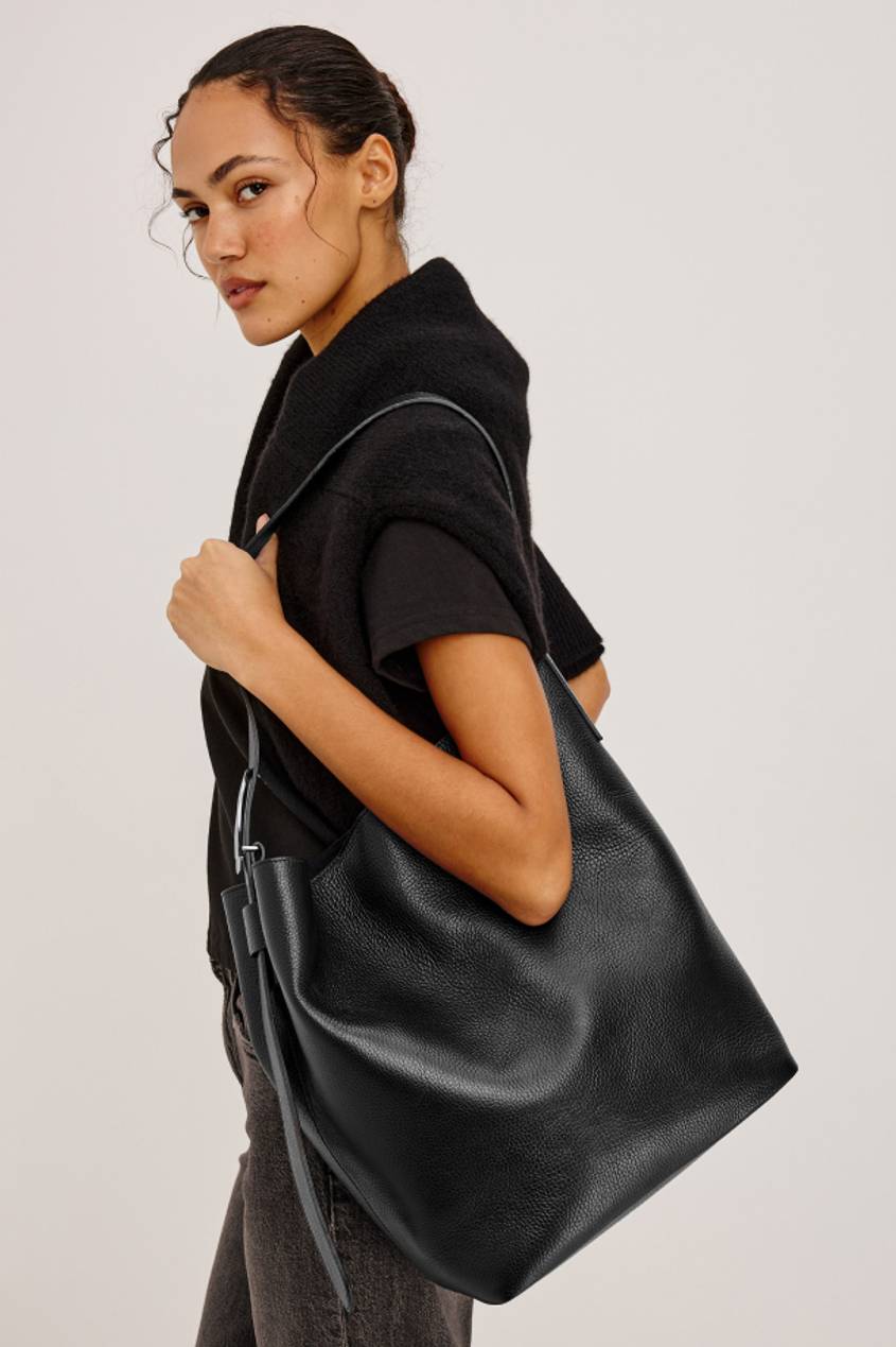 Woman wearing a black top and vest, carrying a large black leather shoulder bag.
