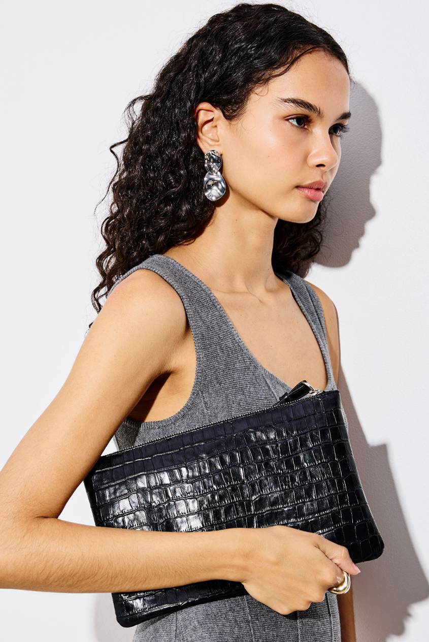 Model wearing a gray knit top and carrying a black croc-textured shoulder bag, paired with silver statement earrings and a gold ring.