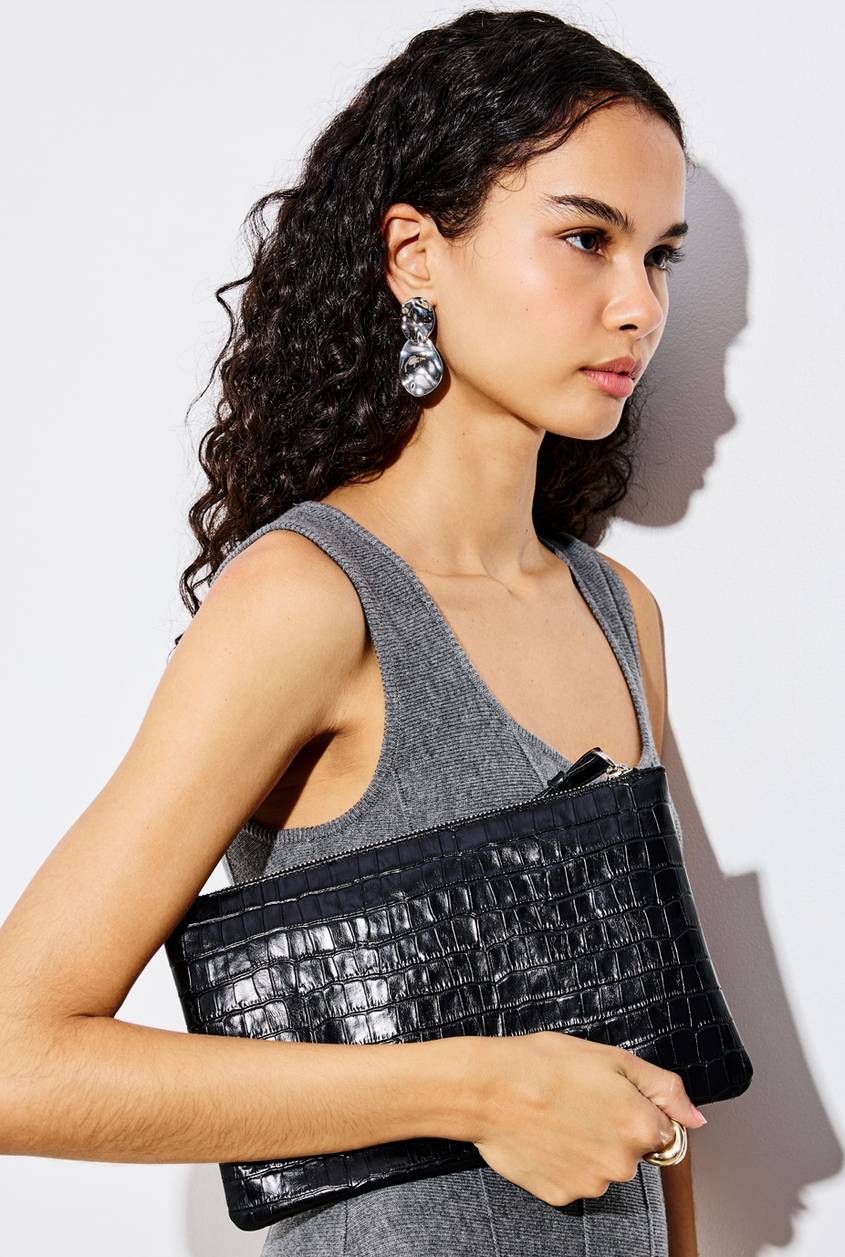 Model wearing a gray knit top and carrying a black croc-textured shoulder bag, paired with silver statement earrings and a gold ring.